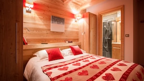 A wooden-paneled bedroom with a bed, a nightstand, a wall-mounted lamp, and a shower area. - Wonderful chalet, 50 m from the slopes (Les Deux-Alpes)
