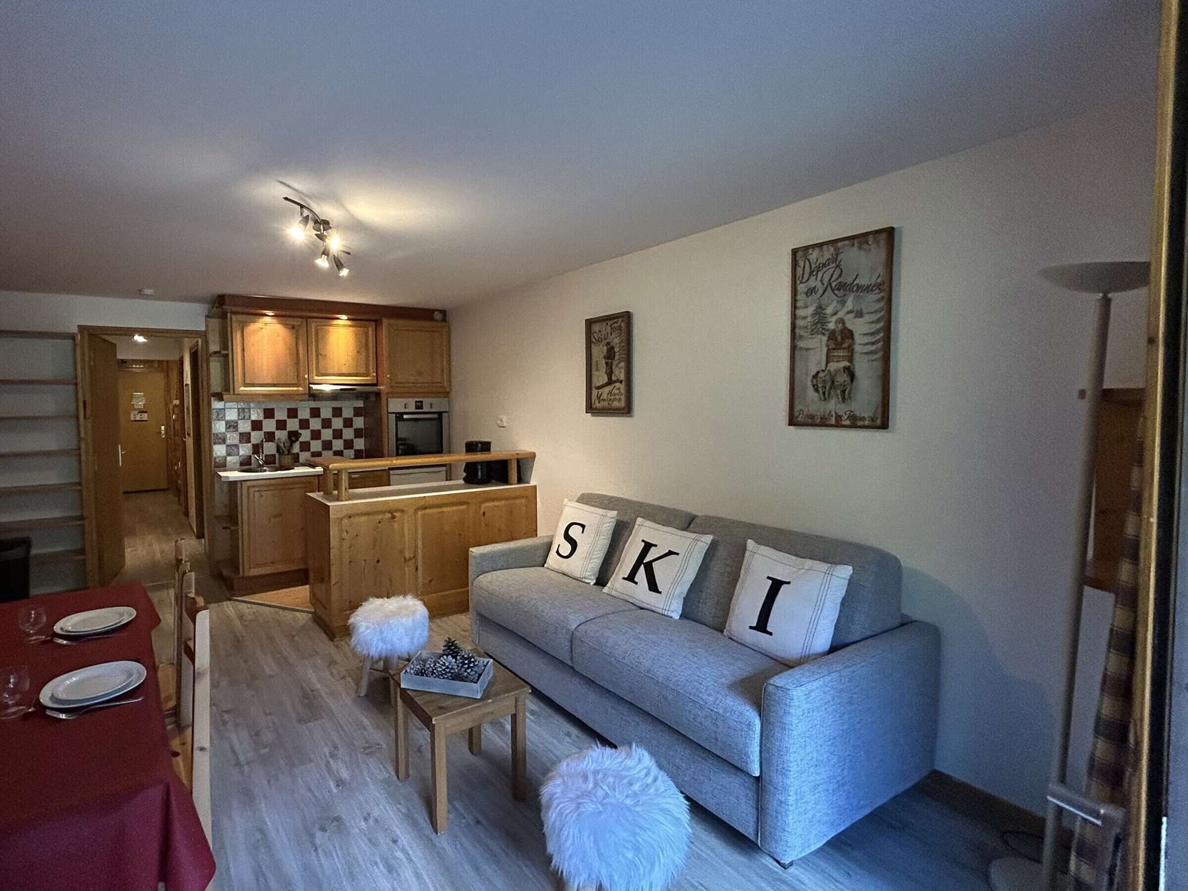 A cozy living room with a sofa, a dining table set for two, and a kitchen in the background.