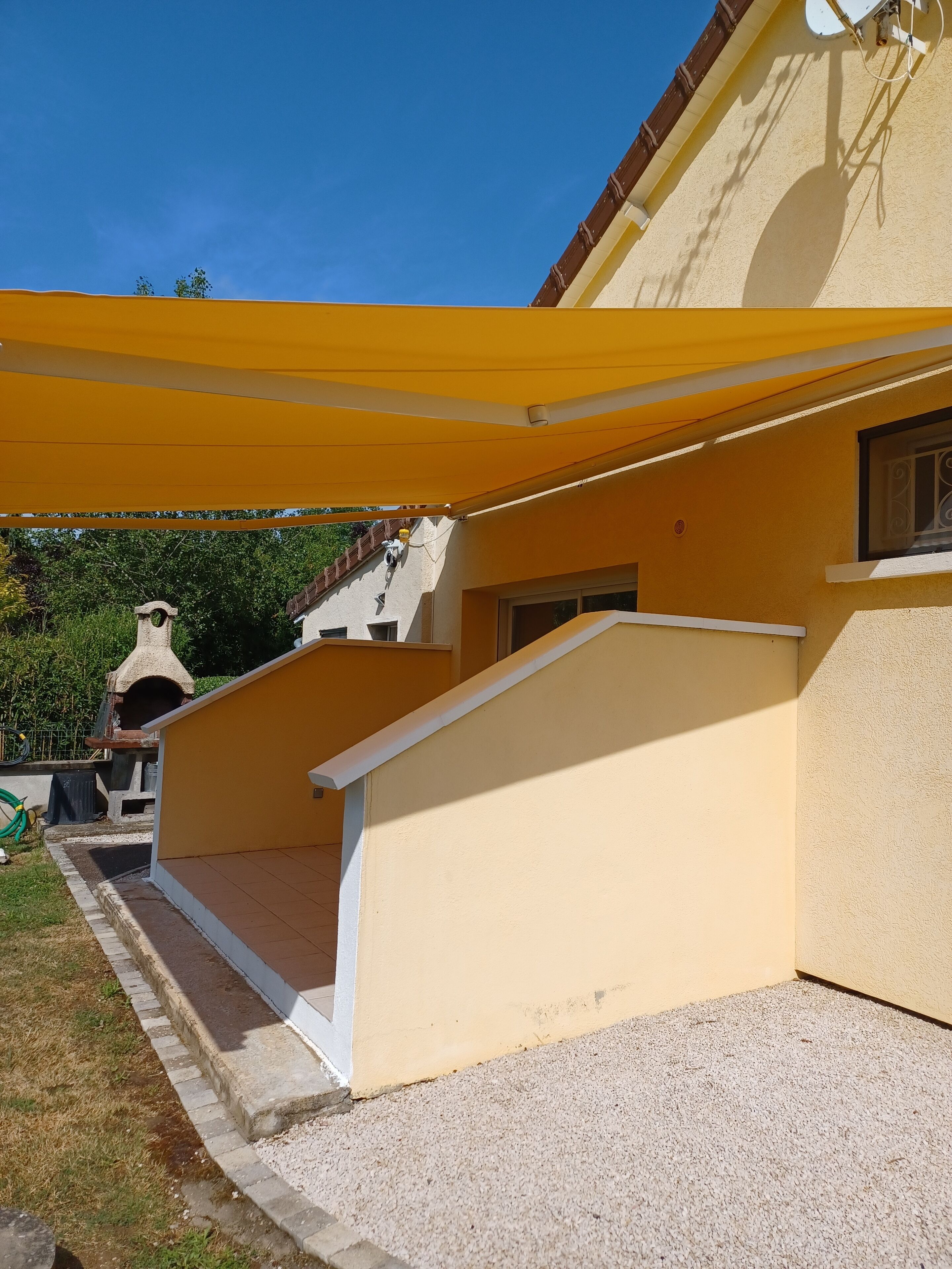 Un espace extérieur abrité, doté d’un auvent jaune, d’un petit escalier et d’un four en pierre.