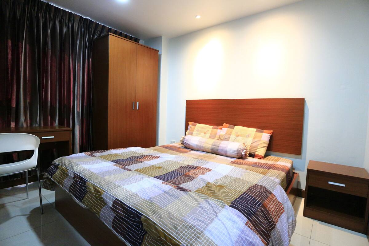 A bedroom with a bed, a wardrobe, a bedside table, and a chair.