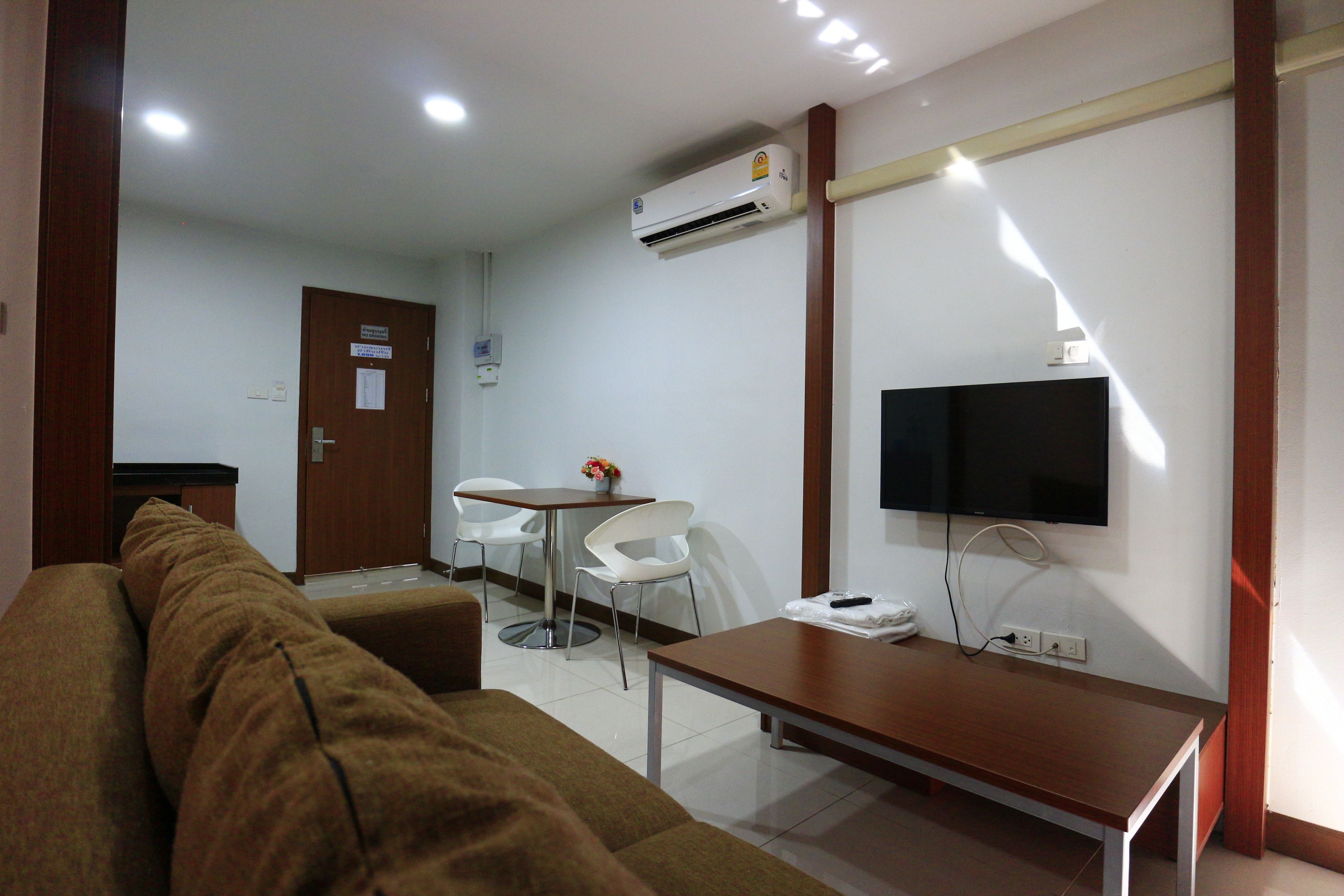 A hotel room with a sofa, a small table, a TV mounted on the wall, and an air conditioning unit.