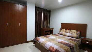 A bedroom with a large wardrobe, a bed with a patterned bedspread, a nightstand, and a bedside table.