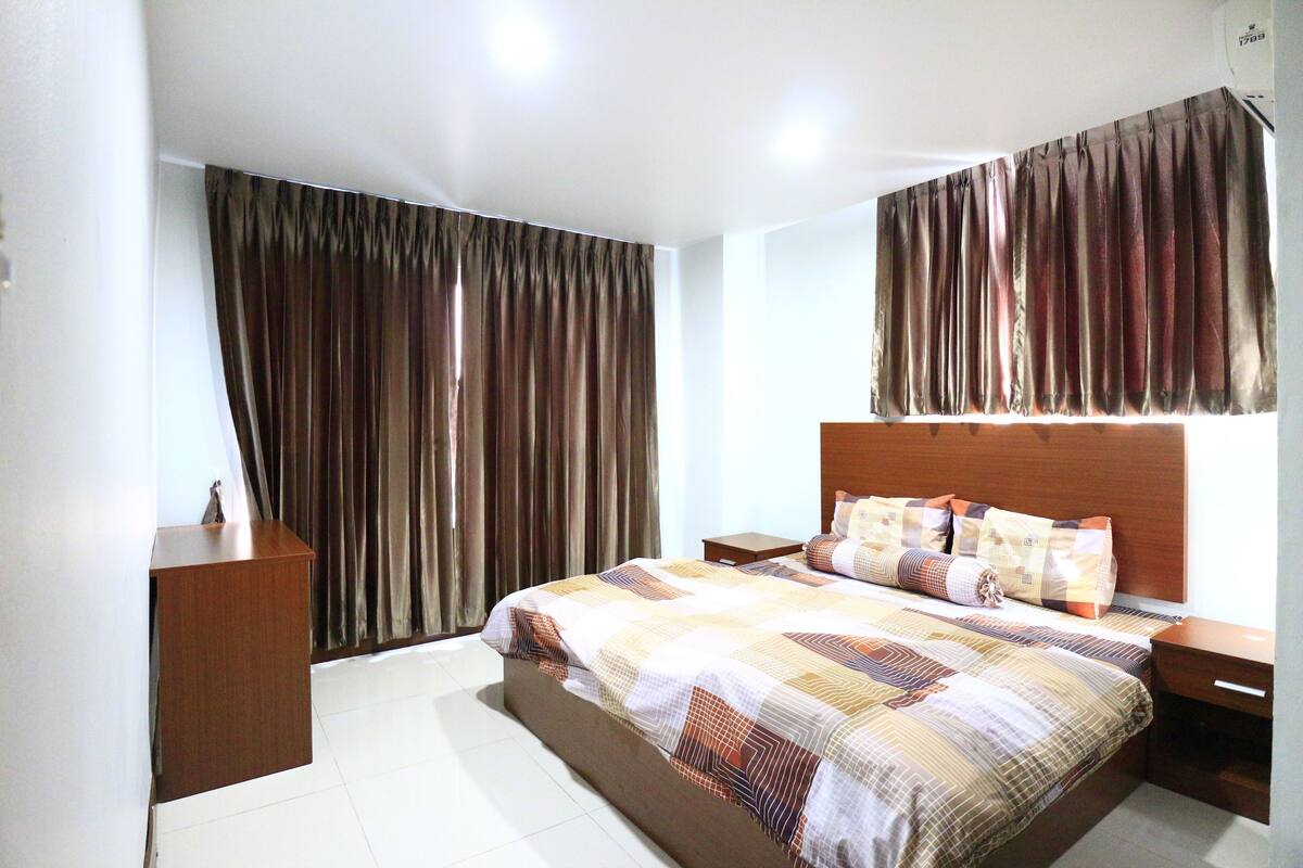 A bedroom with a bed, nightstands, a wooden dresser, and a window with curtains.