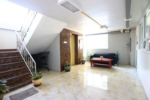 A spacious lobby with a marble staircase, a sofa, a coffee table, and potted plants. - You House Residence (Samut Sakhon)