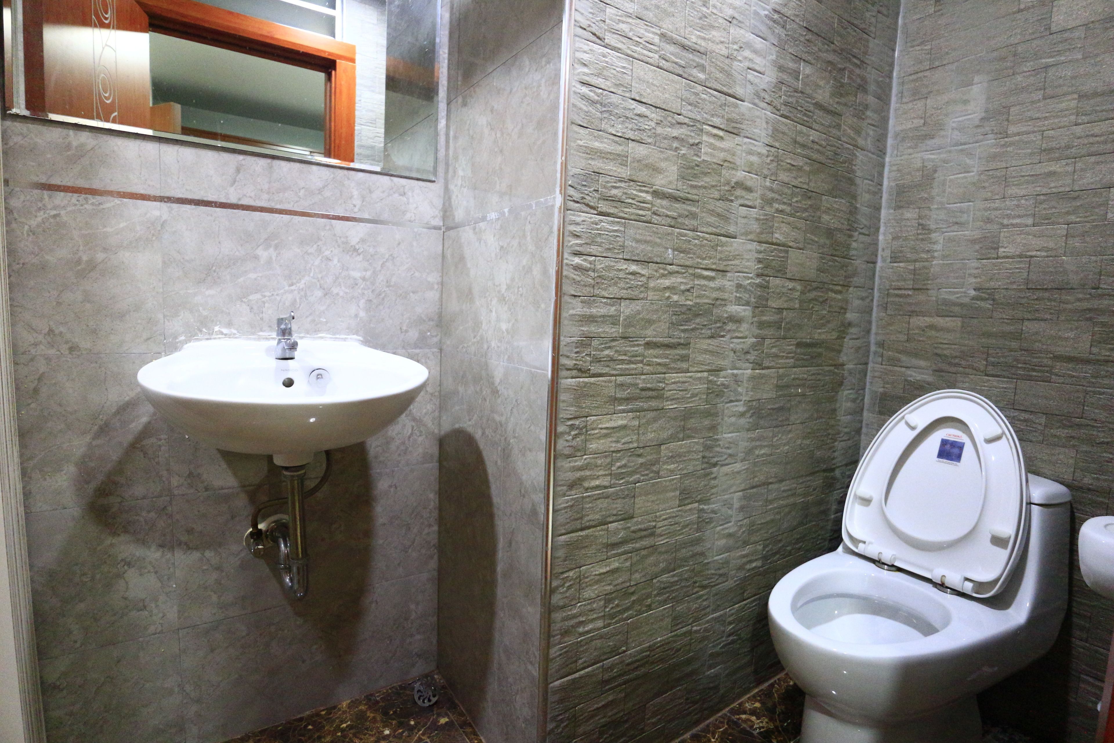 A bathroom with a sink and toilet, marble walls, and a wooden-framed window.