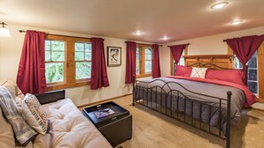 Quarto com cama, mesa de cabeceira, janela com cortinas e vista para o verde lá fora.