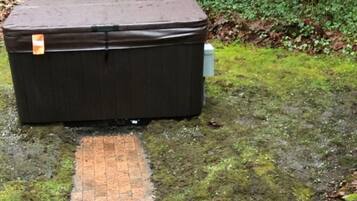 Ein großer, dunkel gefärbter Lagercontainer mit Tragegriff und einem Aufkleber auf der Oberseite, platziert auf moosigem Untergrund neben einem Pflasterweg.