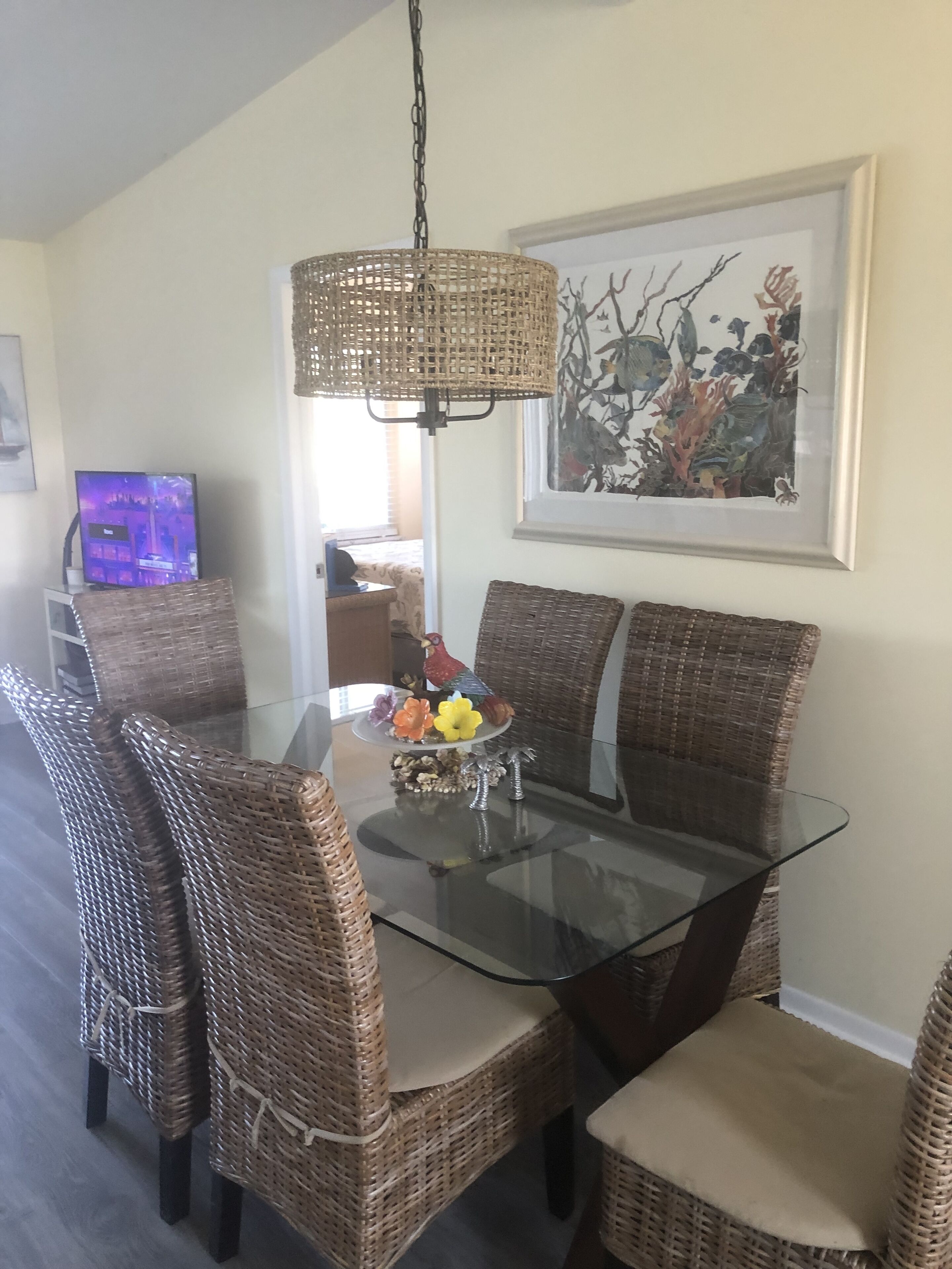 A dining area with wicker chairs, a glass table, and a hanging light fixture.