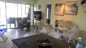 A spacious living area with a glass-top dining table surrounded by wicker chairs, a flat-screen TV, and artwork on the walls. - Best Location for Your best vacation!  (Islamorada, Village of Islands)
