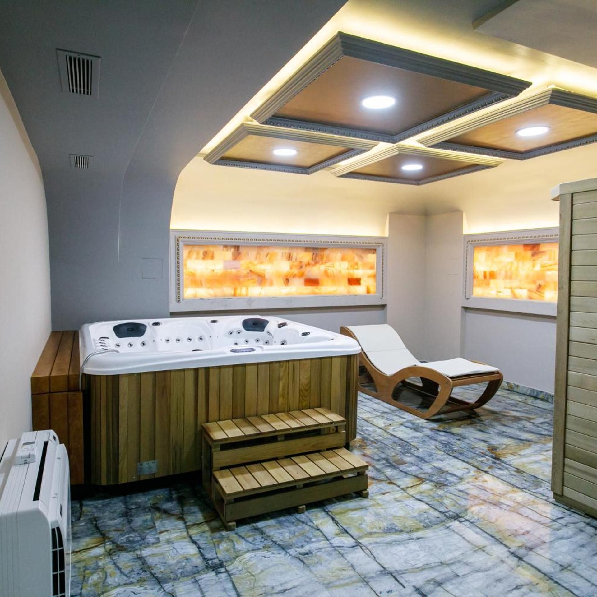 Un cuarto de spa con una bañera de hidromasaje, escalones de madera y dos sillones de descanso.