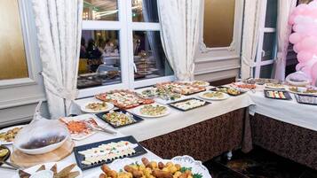 Una mesa de buffet con diversos platos, una araña y cortinas.
