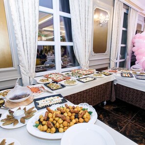 Una mesa de buffet con diversos platos, una araña y cortinas.
