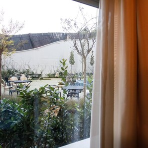 A view of an outdoor patio with tables and chairs, surrounded by greenery and a white wall. - Elite Palace (Tirane)