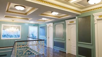 A spacious interior with a marble floor, a staircase with ornate railings, and a view through a window.