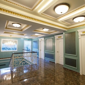 A spacious interior with a marble floor, a staircase with ornate railings, and a view through a window.