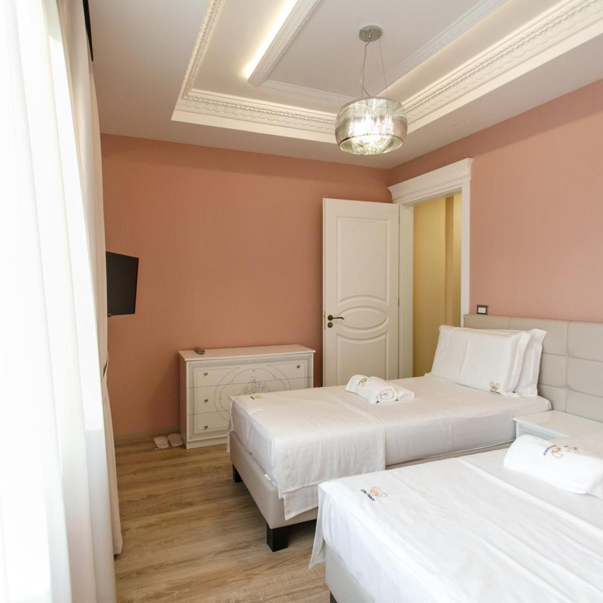 A hotel room with two beds, a dresser, a door, and a chandelier.