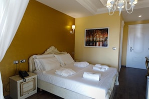 A hotel room with a bed, a painting on the wall, a white door, and a chandelier.