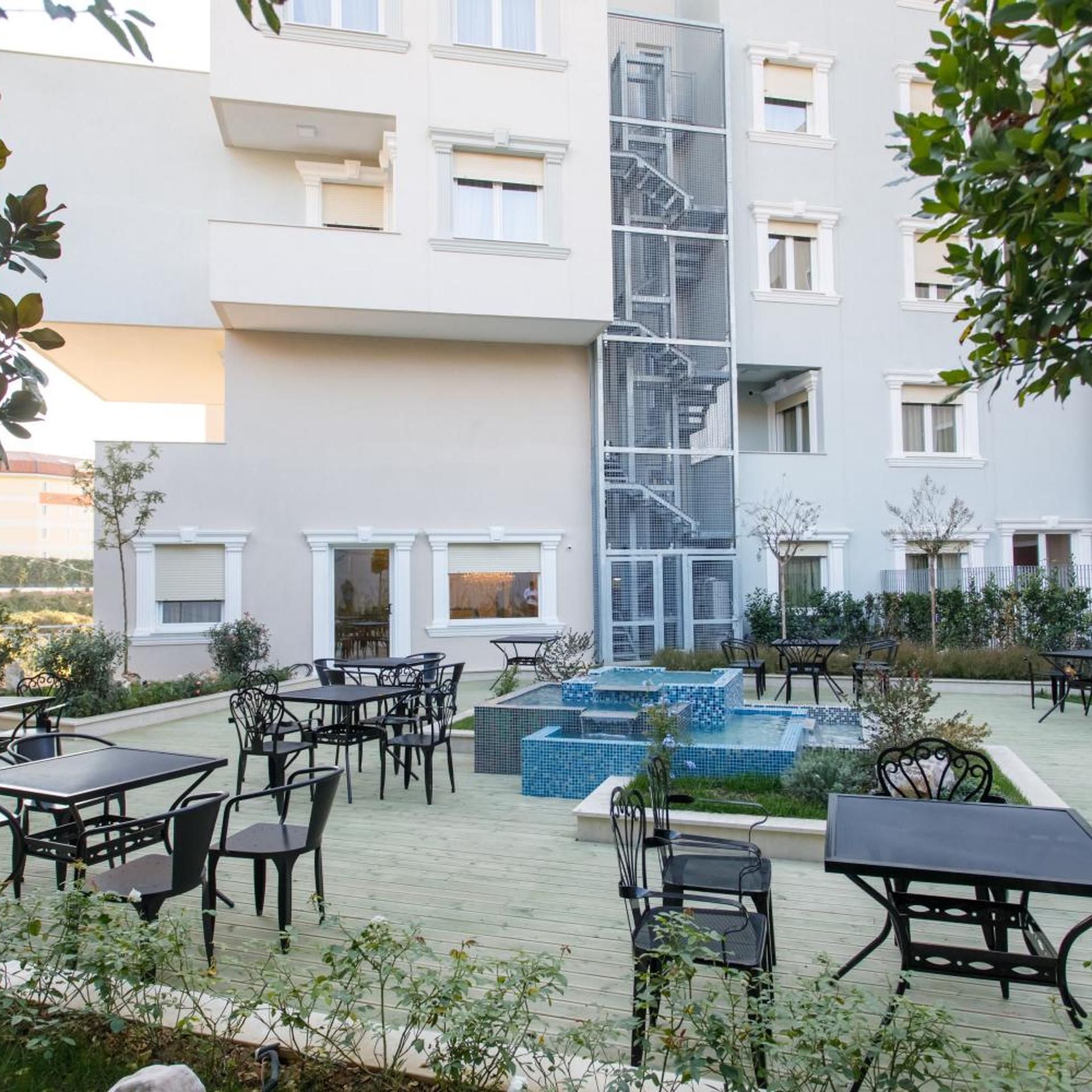 Un patio con mobiliario exterior, una piscina y un edificio con varias ventanas y balcones.