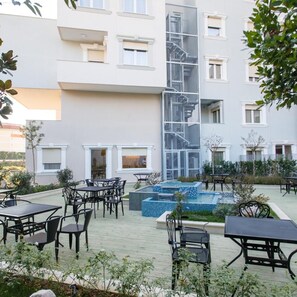 A courtyard with outdoor seating, a pool, and a building with multiple windows and balconies.