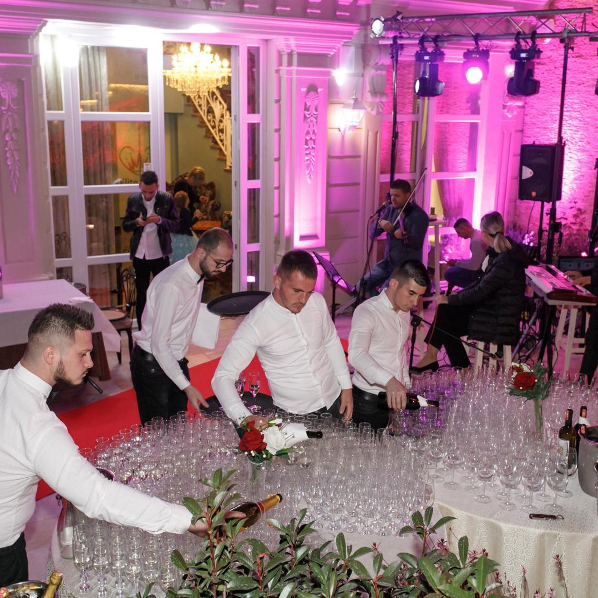 Una habitación con mesas dispuestas para un evento formal, rodeada de invitados.