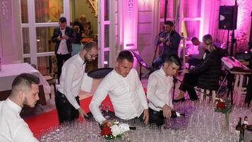 Una habitación con mesas dispuestas para un evento formal, rodeada de invitados.