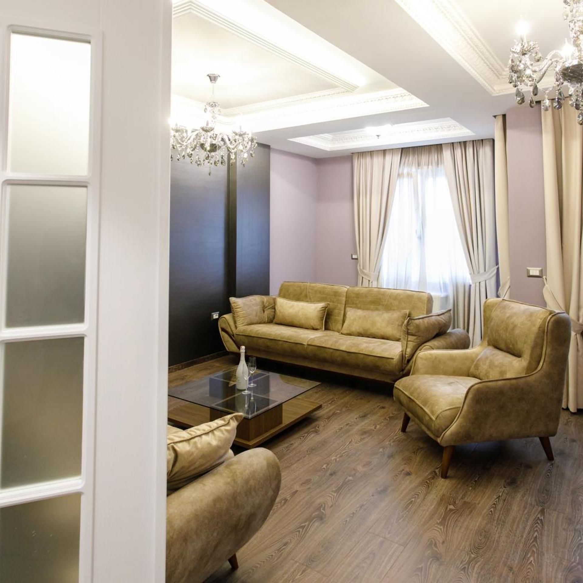 A modern living room with a sectional sofa, armchairs, a glass coffee table, and a chandelier.