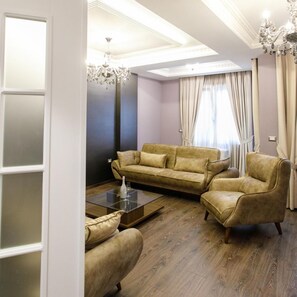 A modern living room with a sectional sofa, armchairs, a glass coffee table, and a chandelier. - Elite Palace (Tirane)