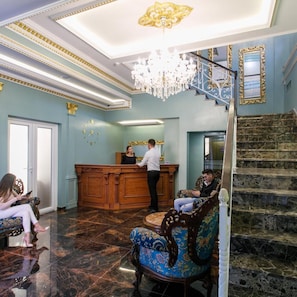 Um hall com balcão de atendimento, lustre, escada e poltrona estampada.