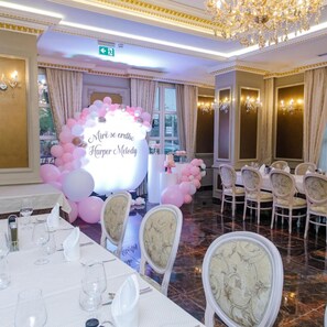 A banquet hall with round tables set for dining, a decorative arch with balloons, and a chandelier. - Elite Palace (Tirane)