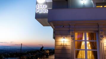 Zona salotto all'aperto con tavoli e sedie, un cartello che riporta 'Elite Palace' e vista del paesaggio sullo sfondo.
