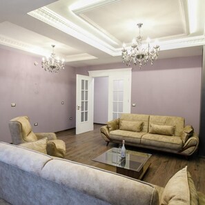 Una sala de estar con un sofá color beige, dos sillones, una mesa de centro de vidrio y una araña.