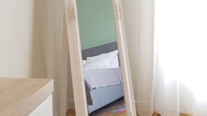 Una habitación con una cama, un espejo de marco blanco y suelo de madera.