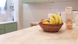 Una cocina con armarios verdes, encimera de mármol, cesta de frutas y cartón de leche.