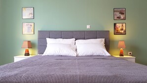 Una cama bien hecha con un cabecero gris, dos lámparas de noche y tres cuadros en la pared.