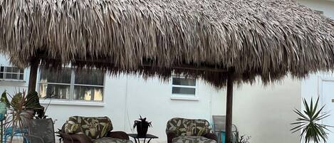 A patio area with a thatched roof, wicker furniture, and potted plants.