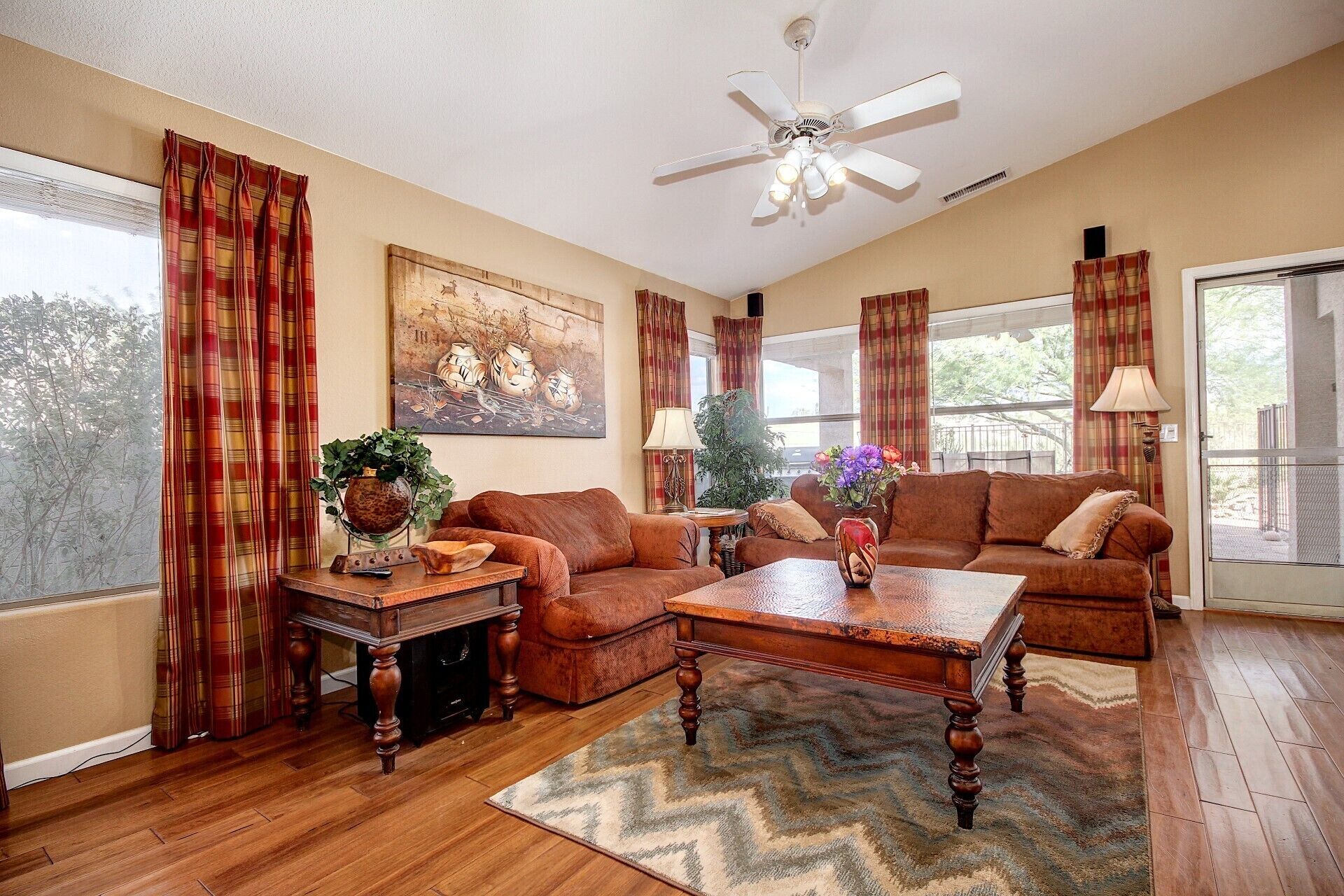 A spacious living room with a brown leather sofa, a wooden coffee table, and a ceiling fan.