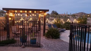 Zona de pati coberta amb llums penjades, mobles d'exterior i una piscina.
