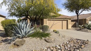 Una propietat residencial amb garatge, una gran planta d'aloi i cactus al jardí.