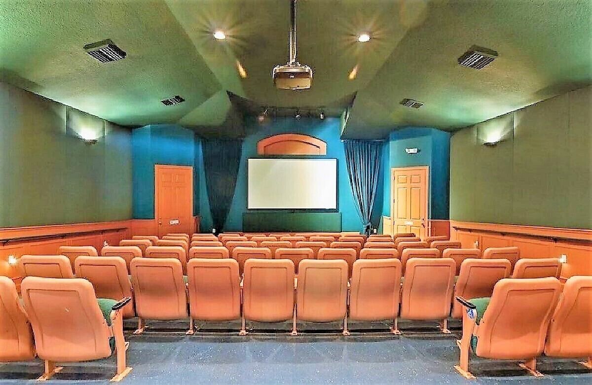 Um teatro com fileiras de assentos laranja, uma tela grande e palco.