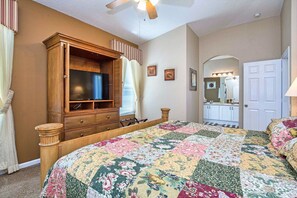 A bedroom with a wooden bed, a television, a wardrobe, and a bathroom visible through an archway. - The Explorer's Club - South Pool/Spa, Gated Area! (Kissimmee)