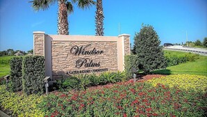 Señal de Windsor Palms, parte de la Comunidad de Parques Verdes, con fachada de piedra rodeada de jardines ajardinados y palmeras.