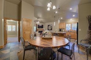 A spacious dining area with a large wooden table, clear chairs, and pendant lighting.
