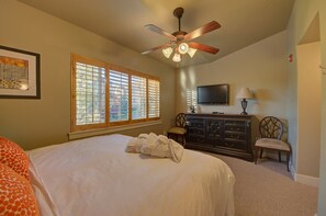Un dormitorio con cama, ventilador de techo, cómoda, televisor y ventana con persianas.