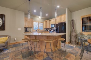 A kitchen with wooden cabinets, a central island with stools, and a dining area with chairs.