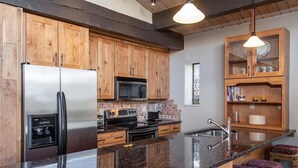 Una cocina con armarios de madera, electrodomésticos de acero inoxidable, encimera de granito y taburetes de bar.