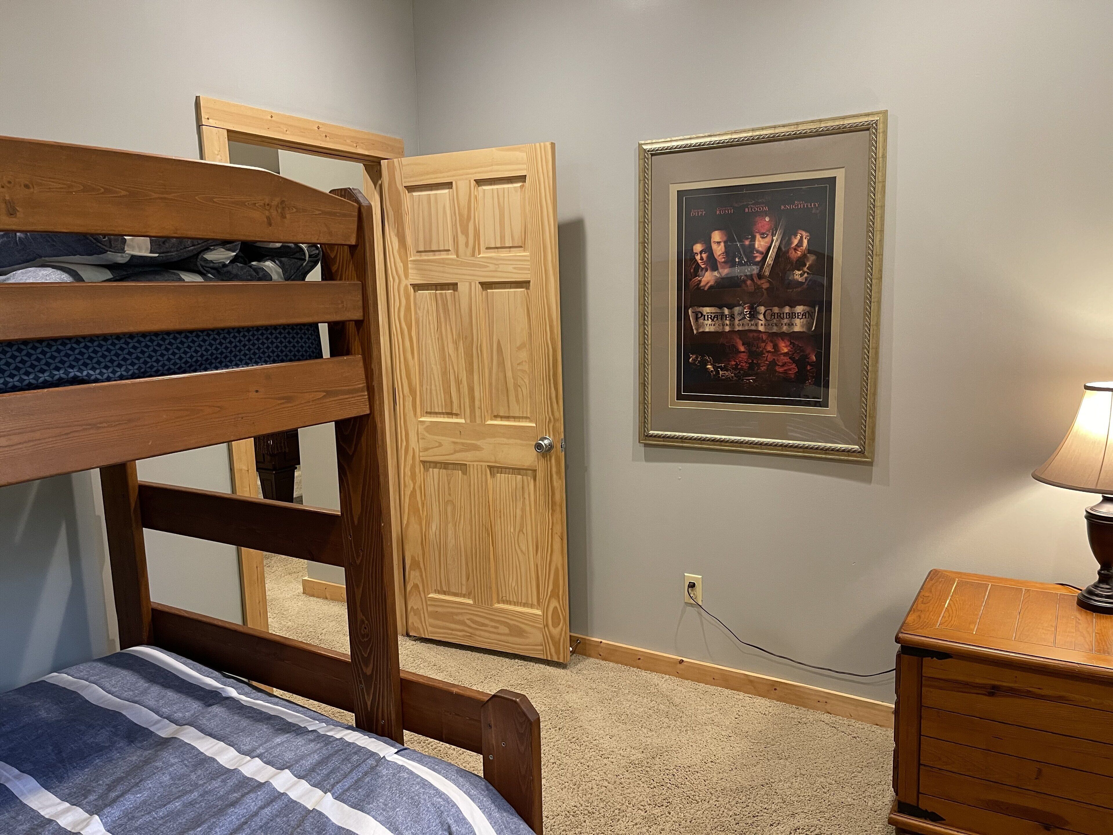 A bedroom with a bunk bed, a wooden door, a framed movie poster, a lamp, and a dresser.