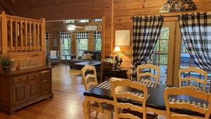 A cozy cabin interior with a dining table, chairs, a sofa, and a wooden cabinet.
