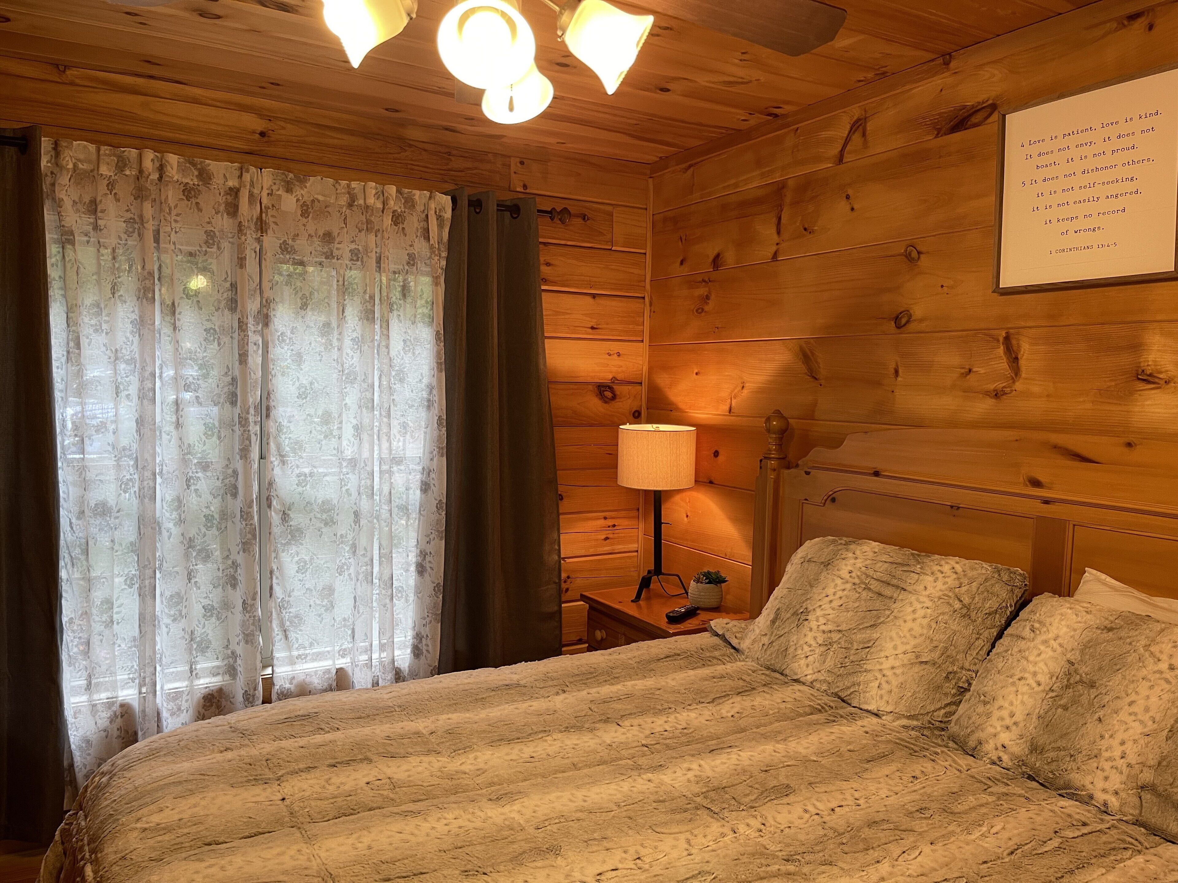 A wooden room with a bed, a nightstand, a lamp, and a wall with a quote.