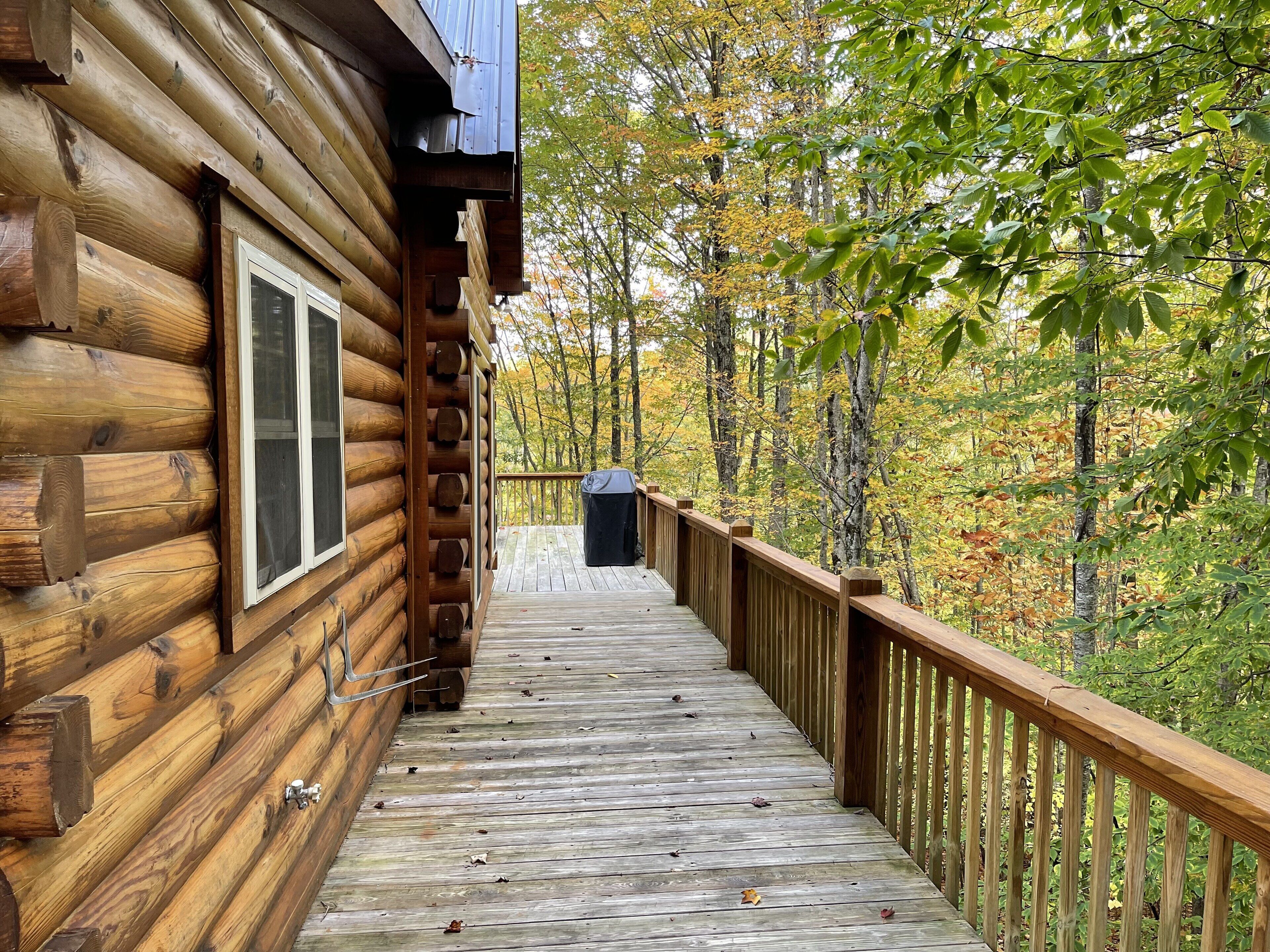A wooden log cabin with a wooden deck leading to a covered outdoor area.