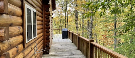 A wooden log cabin with a wooden deck leading to a covered outdoor area.